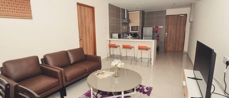 A modern living room with a brown leather sofa, a round coffee table with a magazine and flowers, and a TV on a stand.