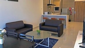 Een moderne woonkamer met twee banken, een glazen salontafel en een eettafel. Achtergrond toont een keuken met een centraal eiland en een televisie.