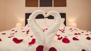 Een bed met een handdoek in de vorm van een hart en rozenblaadjes verspreid over het bed.