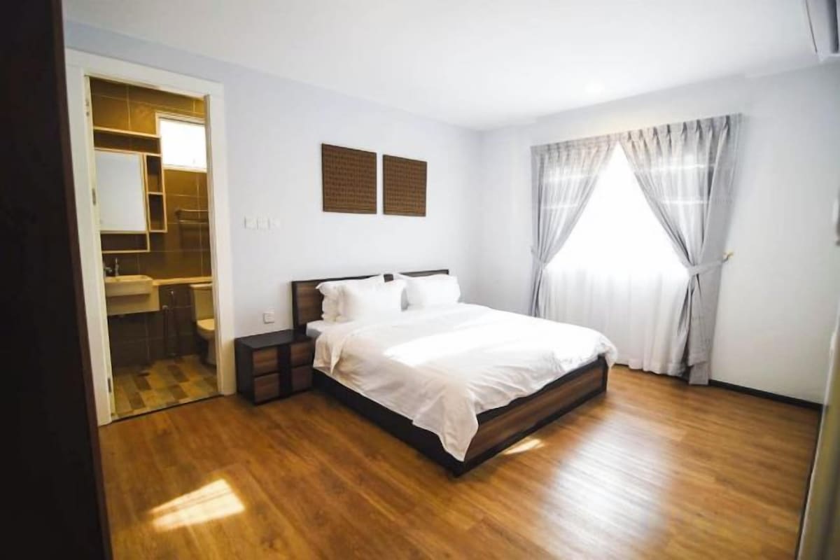 A bedroom with a wooden floor, a bed with white bedding, a nightstand, a mirror, and a window with curtains.