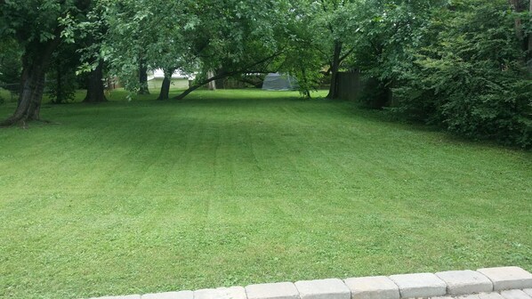 A well-maintained grassy yard with trees and a tent.