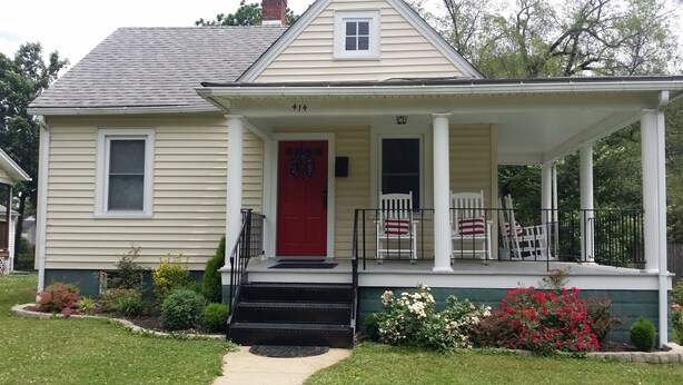 A two-story house with a red door, a porch with white chairs, and a number '414' on the front.