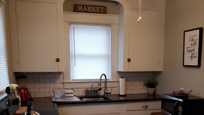 A kitchen with white cabinets, a black countertop, a ceiling fan, a window with blinds, and a sign above the window that reads "MARKET".