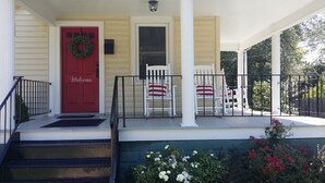 A porch with a red door, white chairs, and a welcome sign.