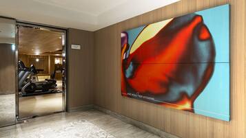 A hotel lobby with a treadmill, a large abstract painting, and a patterned rug.