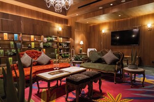 Un hall de hotel acogedor con paneles de madera, un televisor de pantalla plana grande, asientos cómodos y diversas plantas decorativas.