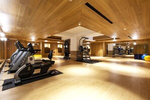 Ein großzügiger Fitnessraum mit Holzboden, Laufbändern und Kurzhanteln.