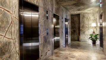 A hallway with marble walls and floors, featuring three elevators and a potted plant.