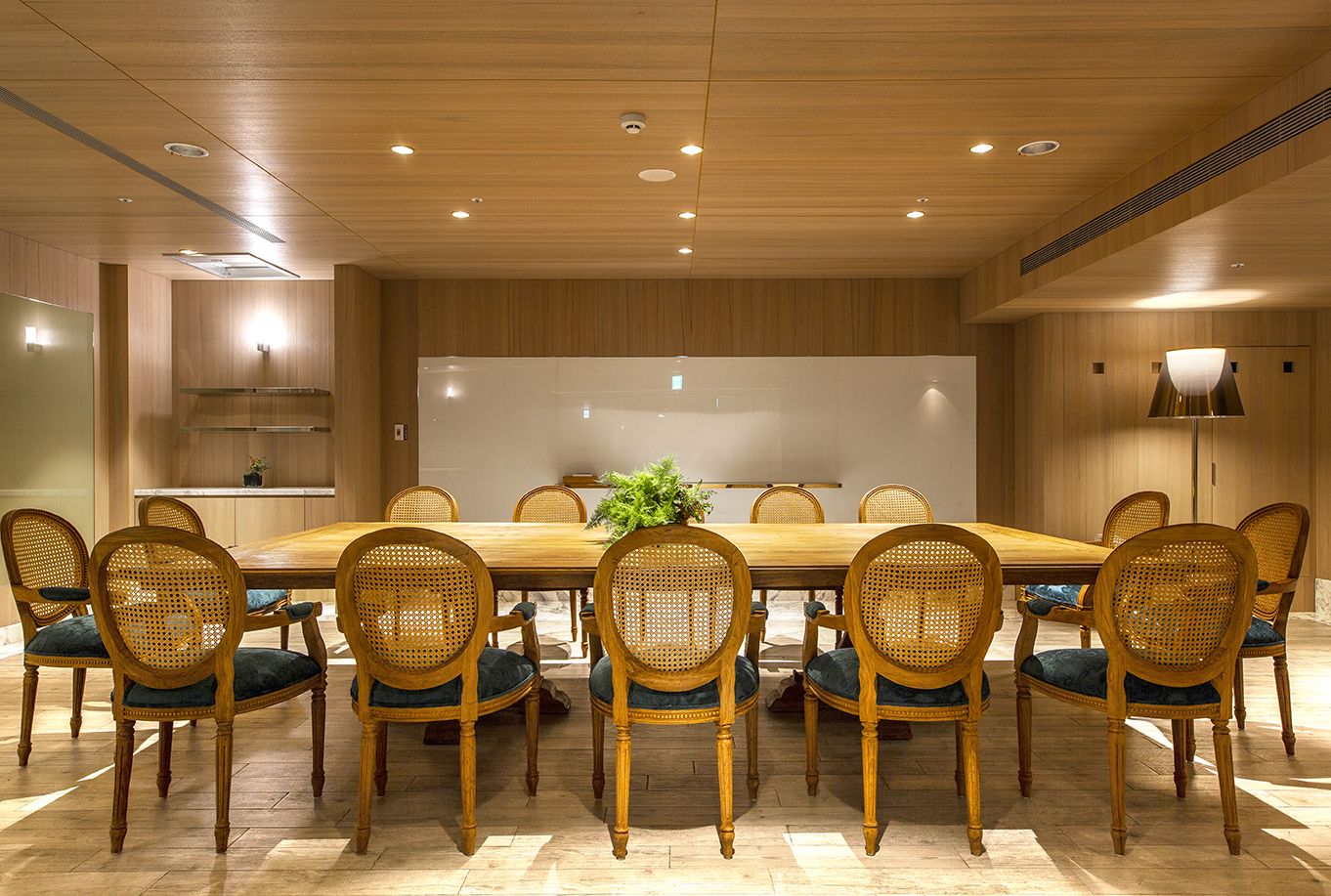 A conference room with a large wooden table surrounded by wicker chairs with blue cushions.