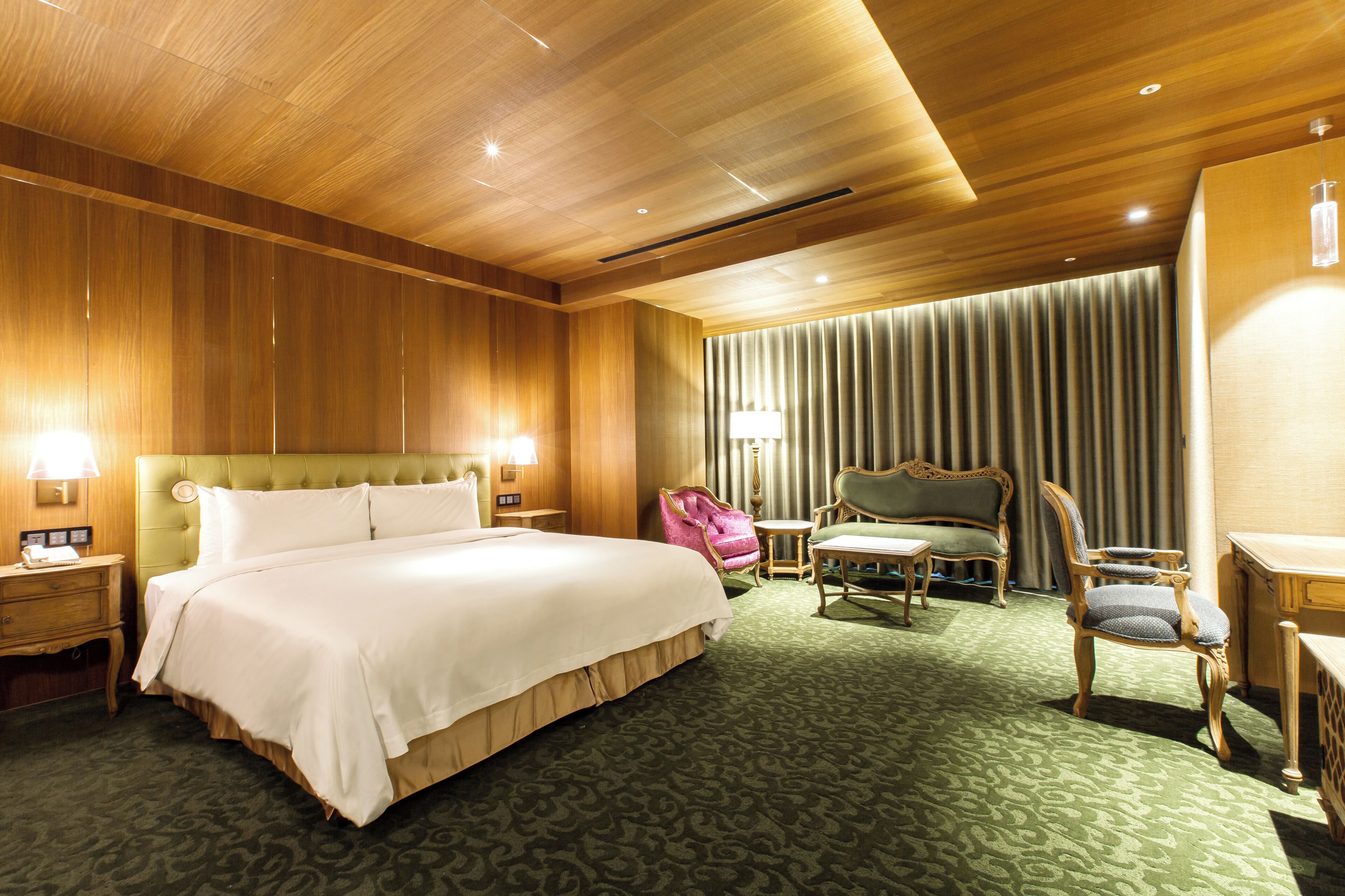 A hotel room with a large bed, two chairs, a small table, and a lamp.