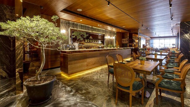 A restaurant with a wooden bar, green upholstered chairs, and a large potted tree. - Inhouse Hotel Grand (Taichung)