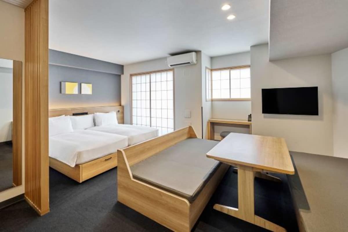 A modern hotel room with a bed, two bedside tables, a desk, and a TV.