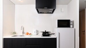 A modern kitchen with a black range hood, a microwave, a white refrigerator, and a sink with a kettle and oranges on the counter. - MIMARU Tokyo Ueno Inaricho (Tokyo)