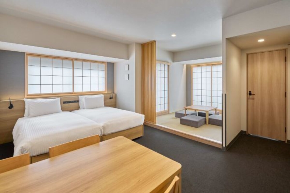 A hotel room with two beds, a wooden table, and a small seating area with cushions.