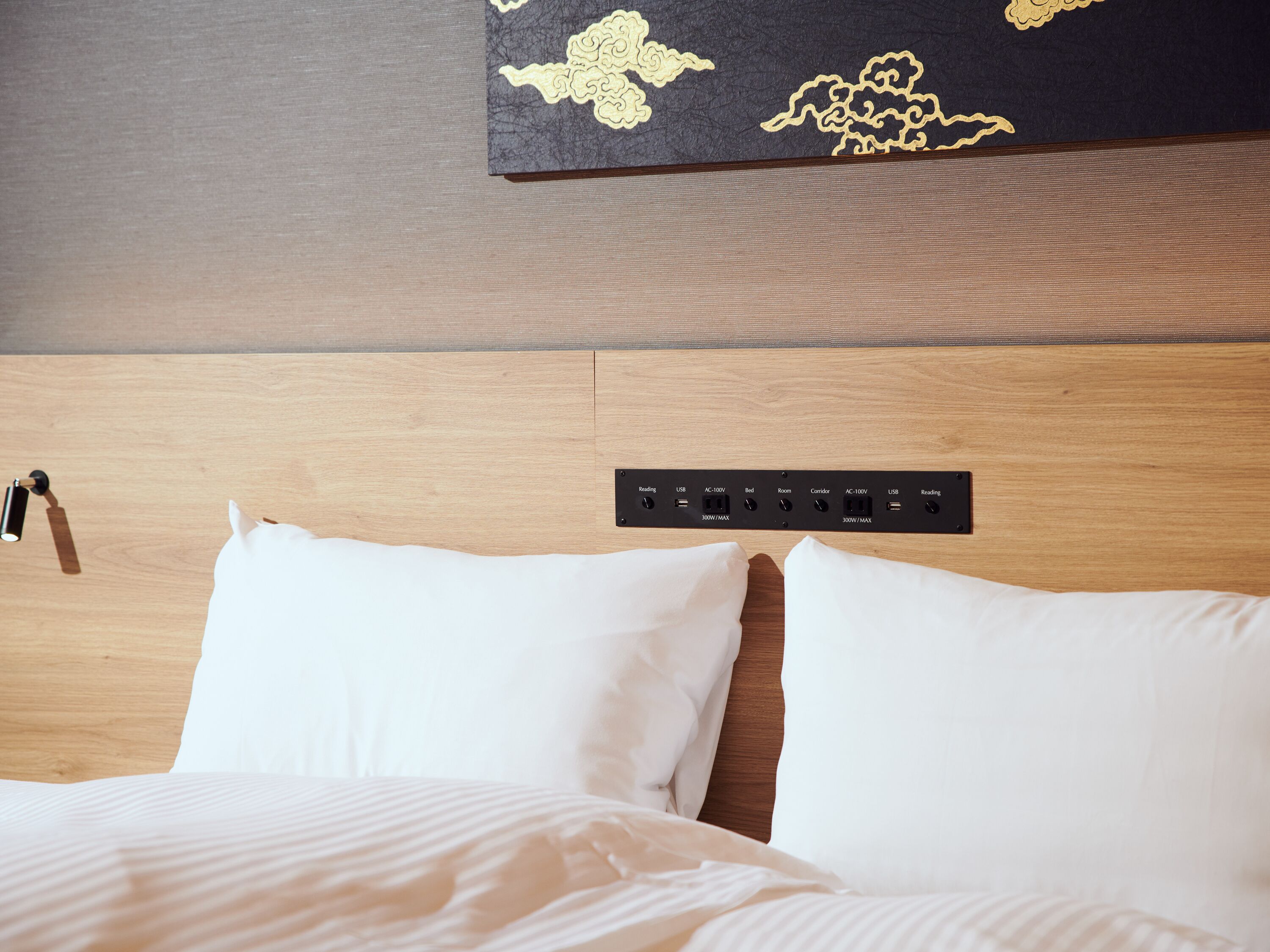 Habitación de hotel con cabecera de madera, regleta con varios enchufes y una obra de arte colgada en la pared.