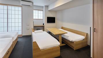 A modern hotel room with two single beds, a wooden desk, a chair, a TV mounted on the wall, and a sliding door leading to a balcony.