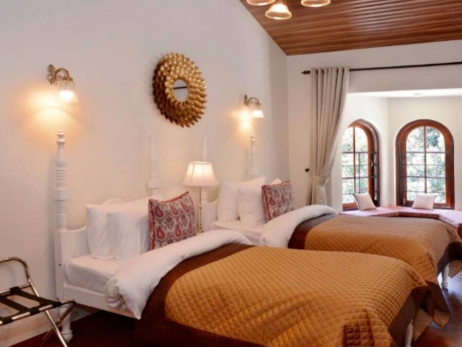 A hotel room with two beds, a wooden ceiling, and large arched windows.