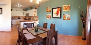 A dining area with a wooden table and chairs, a vase with flowers, and artwork on the wall. - VillaNicky Rincon, PR 2,800 Sqft Beach Front Oasis  (Rincon)