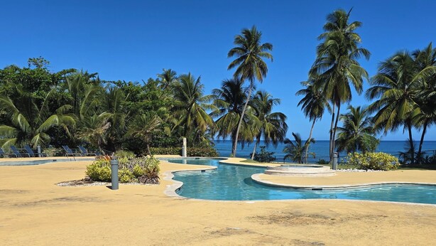 A resort pool area with multiple swimming pools, palm trees, and a view of the ocean. - VillaNicky Rincon, PR 2,800 Sqft Beach Front Oasis  (Rincon)