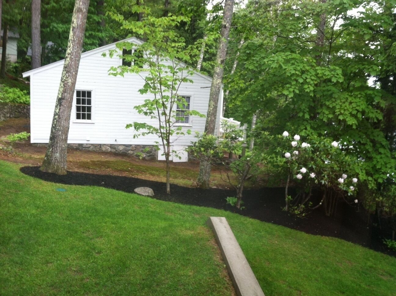 Une maison blanche avec un petit jardin, une terrasse en bois et un arbre aux fleurs blanches.