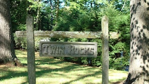 Un letrero de madera con el texto "Twin Rocks" en un entorno natural con árboles y césped.