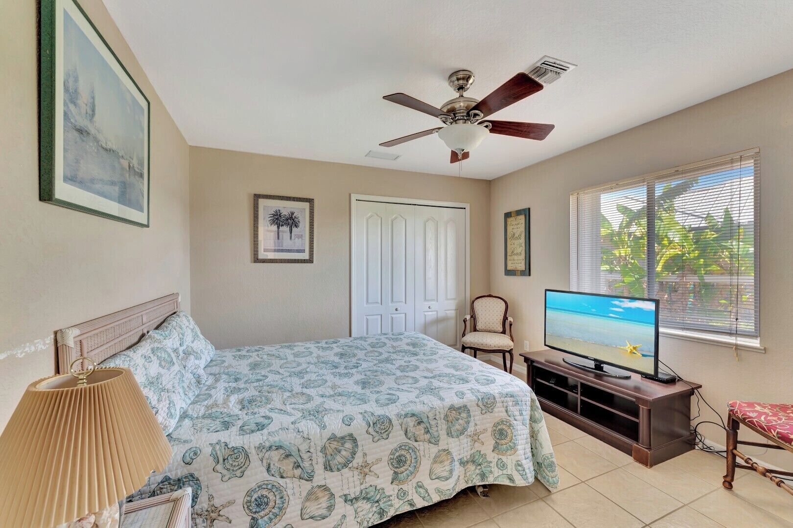 A bedroom with a bed, a ceiling fan, a TV, a chair, and a window with blinds.