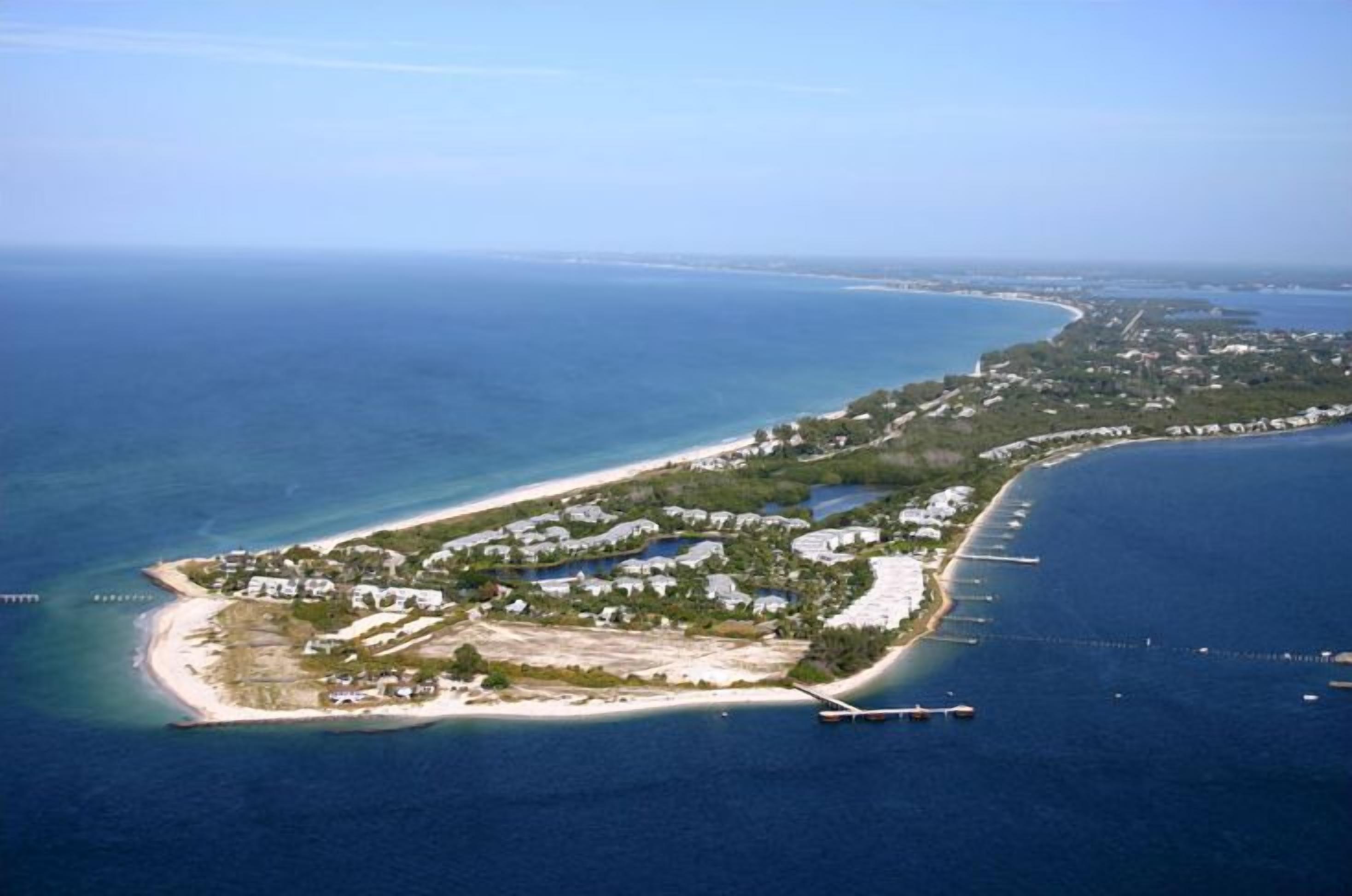 Vista aèria d'una propietat costanera amb una extensa platja, una marina i un grup d'edificis.