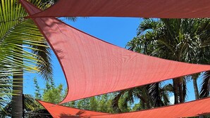 Un espace patio doté d’un sol en briques, de mobilier d’extérieur et d’une voile d’ombrage rouge.