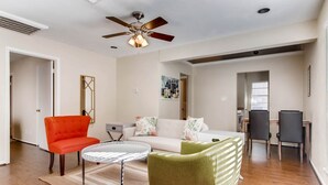 A spacious living room with a ceiling fan, a white sofa, a green armchair, and a small round table. - Katy Trail Cosy and Elegant (Dallas)