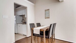 A dining area with a wooden table, four chairs, and a kitchen in the background. - Katy Trail Cosy and Elegant (Dallas)