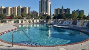 Ein Pool mit gewölbter Kante, umgeben von Liegestühlen und einem Metallzaun.