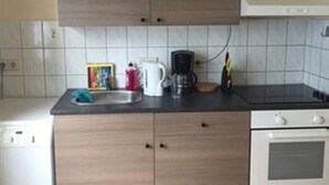 A kitchen with a dishwasher, stove, and countertop with a coffee maker, kettle, and other small appliances.