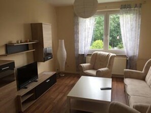 A living room with a sofa, a coffee table, a TV, and a lamp. - Monteurwohnungen Netzel (Penkun)