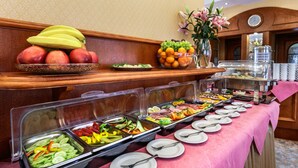 Un buffet proposant une variété de plats, notamment des fruits, des légumes et des viandes, disposés sur une table recouverte d’une nappe rose.