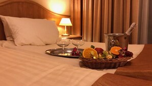 Une chambre d’hôtel avec un lit bien fait, une table de chevet avec une lampe, un plateau avec des verres et un panier de fruits.