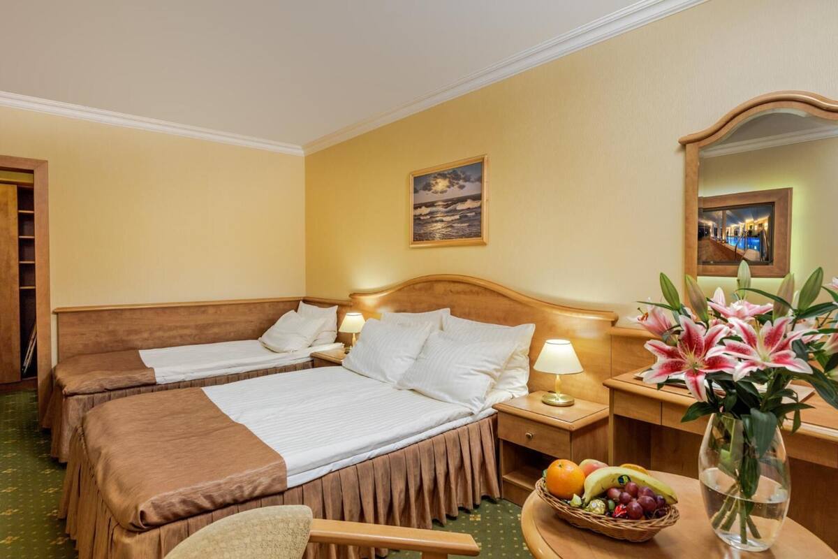 Une chambre d’hôtel avec deux lits, un bureau avec une lampe, un miroir, un tableau et un vase de fleurs.