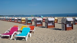 Une plage bordée de rangées de chaises de plage et de parasols, dont certains sont dotés de toiles rayées et d’autres de toiles d’une couleur unie.