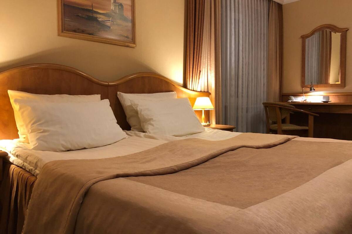 Une chambre d’hôtel avec un grand lit, un bureau avec une chaise, une lampe et un tableau au mur.