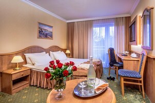 A hotel room with a bed, a desk, a chair, a vase with red roses, a bottle of Cointreau, and a tray with a glass and a napkin.
