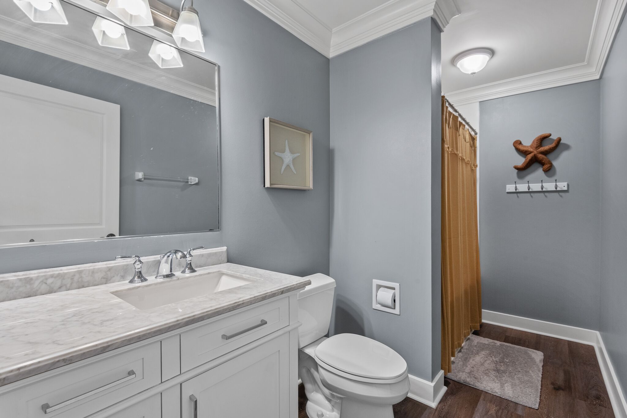 A bathroom with a white vanity, a large mirror, a toilet, and a starfish decoration on the wall.