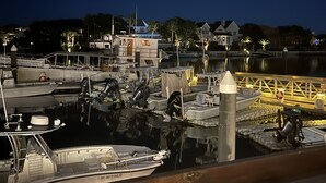 Un port de plaisance de nuit, avec des bateaux amarrés, une jetée en bois et des bâtiments en arrière-plan.
