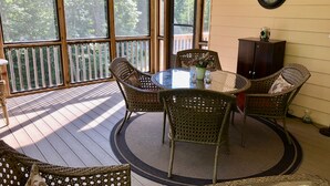 A covered patio with a round table and wicker chairs, surrounded by a wooden deck and large windows. - Center Hill Lake, family/pet friendly custom home on 3-acre lot, 8-10 pers. (Smithville)