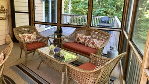 A covered porch with wicker furniture and a glass table, overlooking a wooden deck and greenery. - Center Hill Lake, family/pet friendly custom home on 3-acre lot, 8-10 pers. (Smithville)