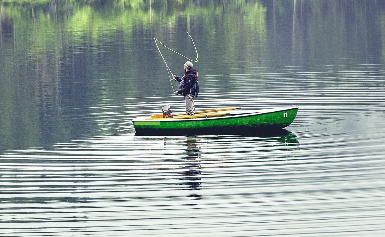 Uma pessoa pesca de um pequeno barco verde em águas calmas.