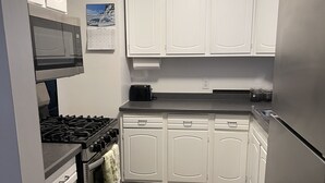 Una cocina con armarios blancos, un refrigerador de acero inoxidable, un microondas, una estufa y un calendario en la pared.