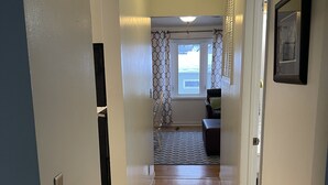 Un pasillo con suelo de madera, una lámpara en el techo, una puerta con espejo y una ventana con cortinas estampadas.