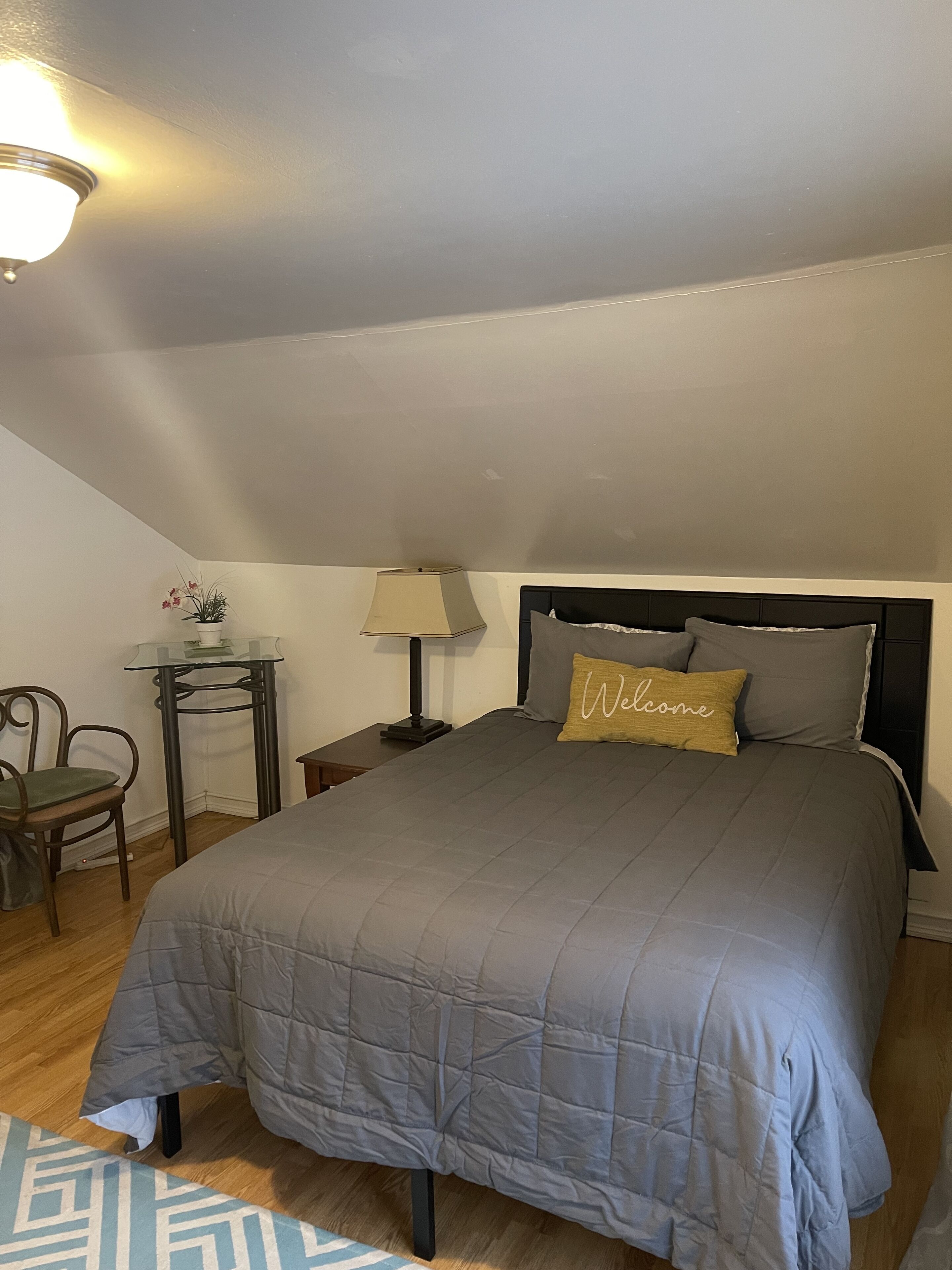 Un dormitorio con una cama, una mesita de noche, una lámpara, una silla y una pequeña mesa con una planta.