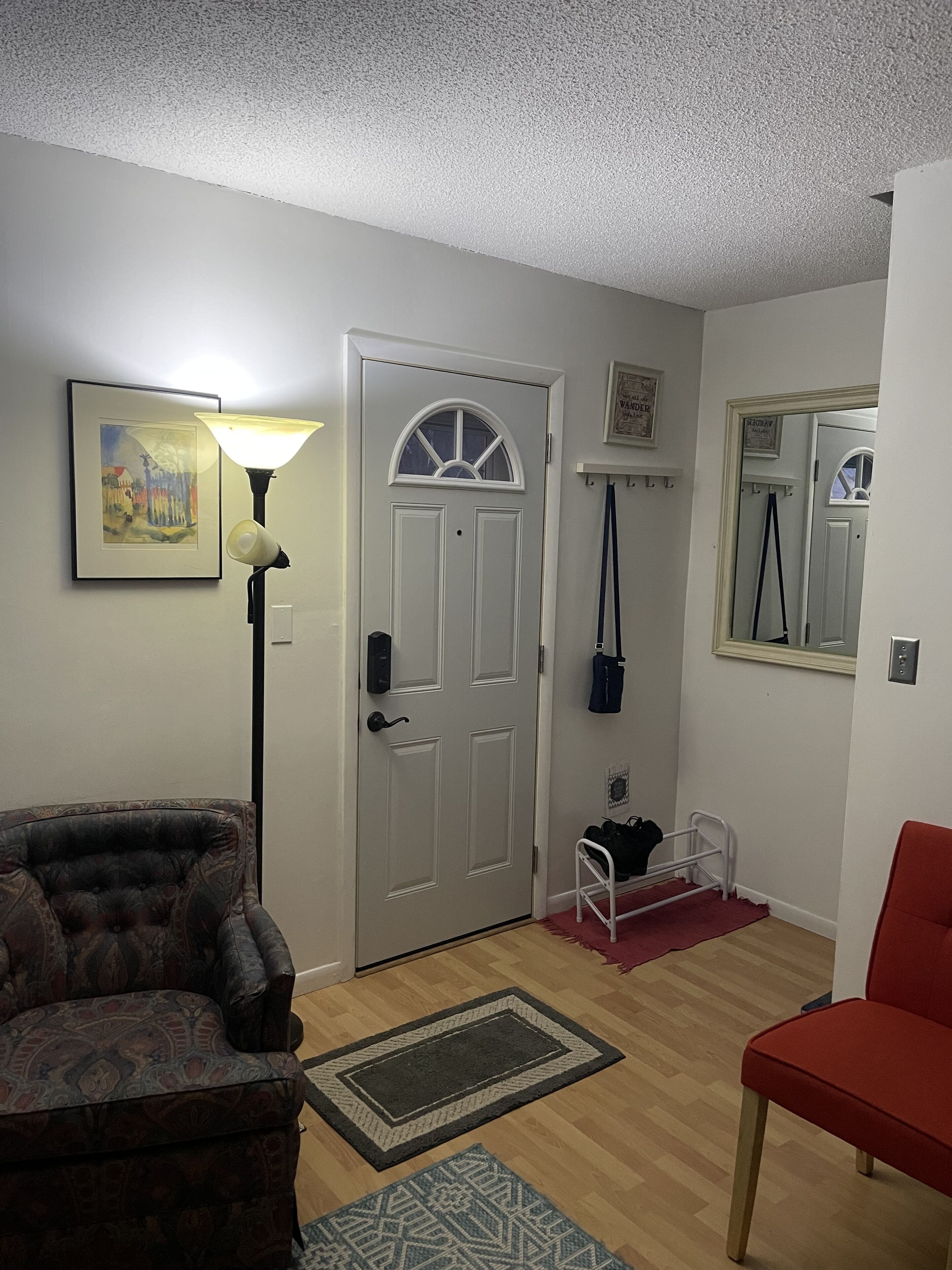 A living room with a door, a lamp, a chair, a rug, and a coat rack.