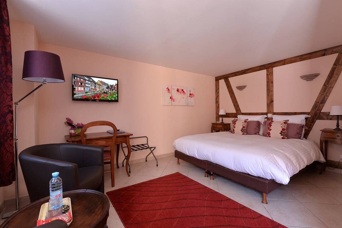 A bedroom with a bed, a desk, a chair, a TV, and a lamp.