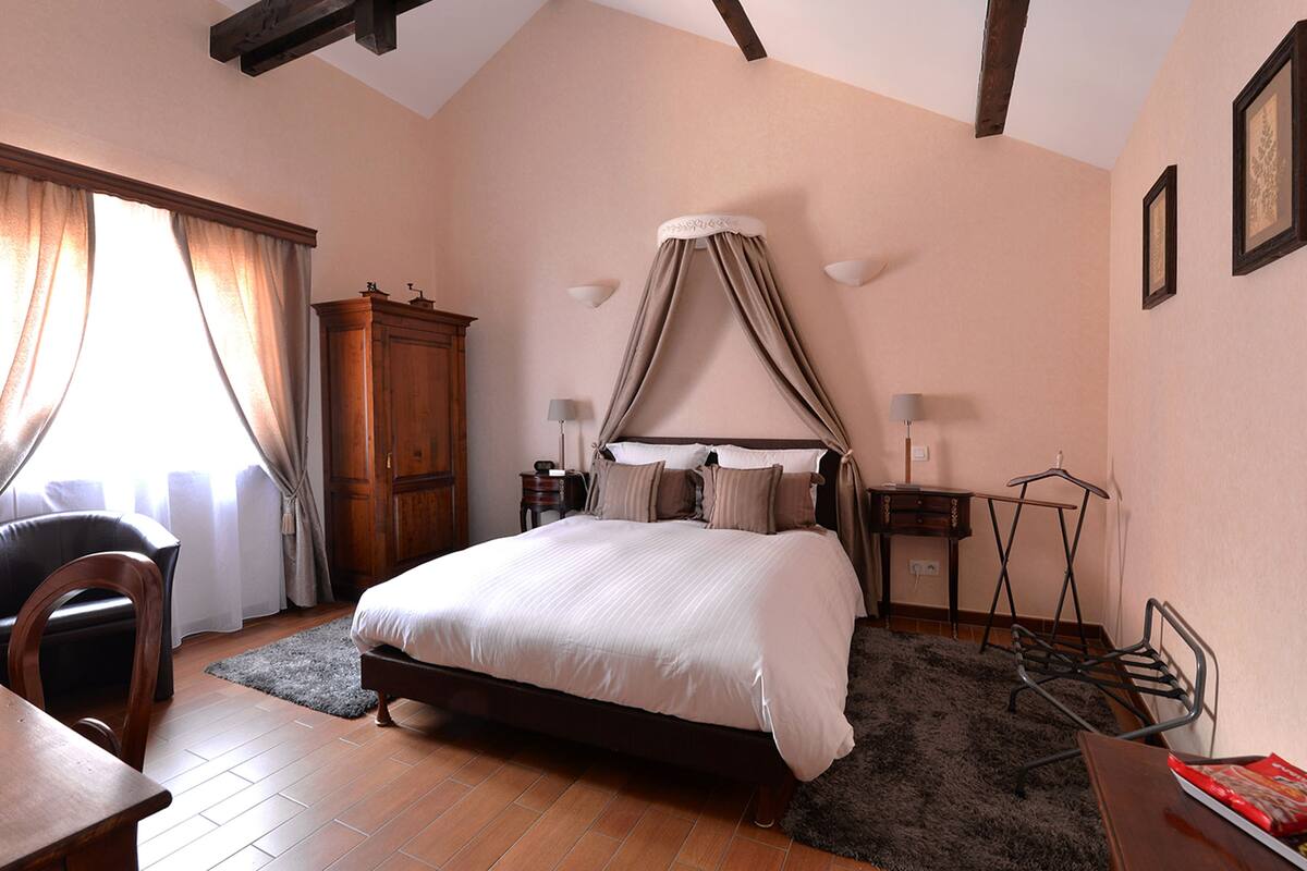 A bedroom with a large bed, a wooden wardrobe, a desk, and a chair.